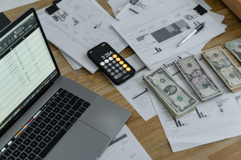 Payroll Demystified: More Than Just Cutting Checks A desk with financial documents, currency, a laptop, and phone calculator.